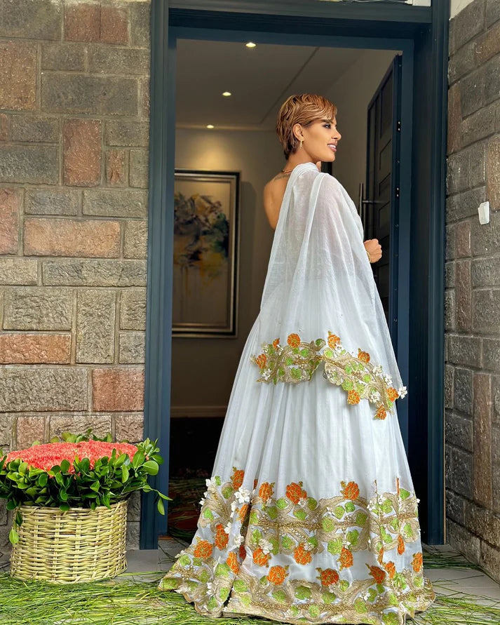 captivating green and orange Habesha dress, a masterpiece of handcrafted artistry, is adorned with delicate floral and cross-stitch embroidery.