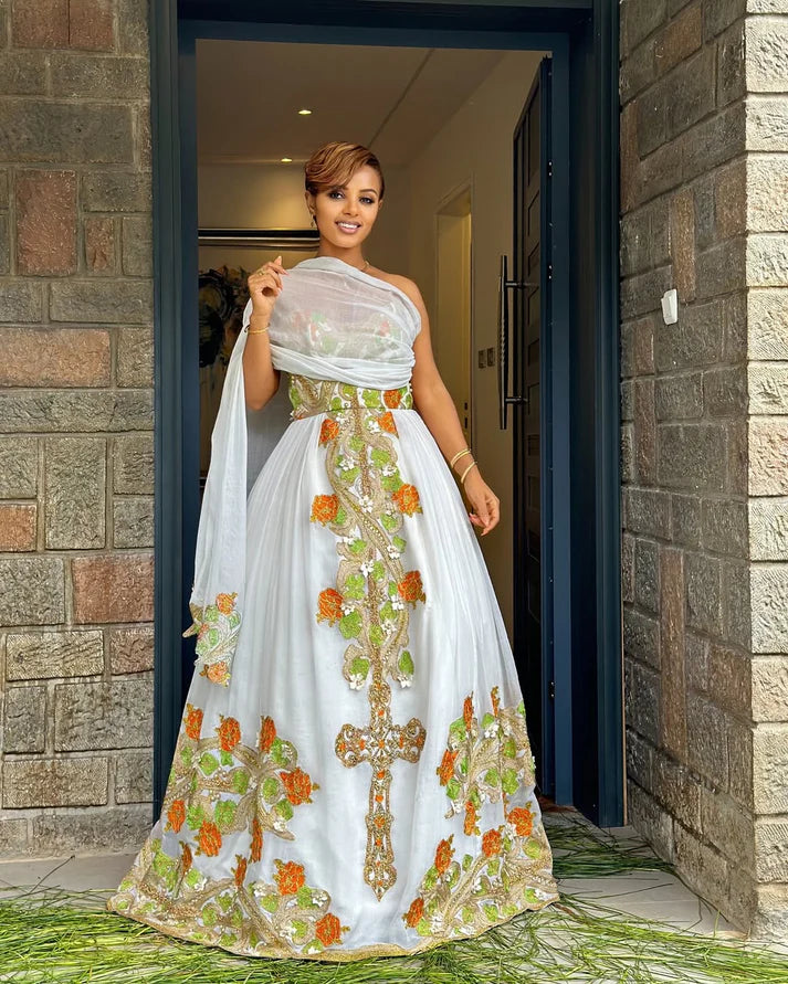 captivating green and orange Habesha dress, a masterpiece of handcrafted artistry, is adorned with delicate floral and cross-stitch embroidery.