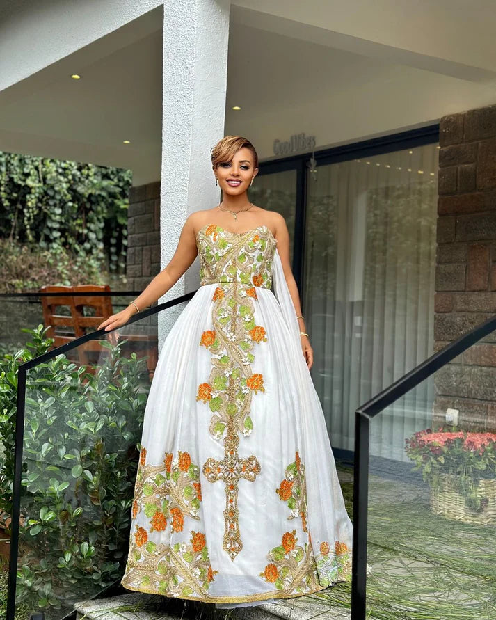 captivating green and orange Habesha dress, a masterpiece of handcrafted artistry, is adorned with delicate floral and cross-stitch embroidery.